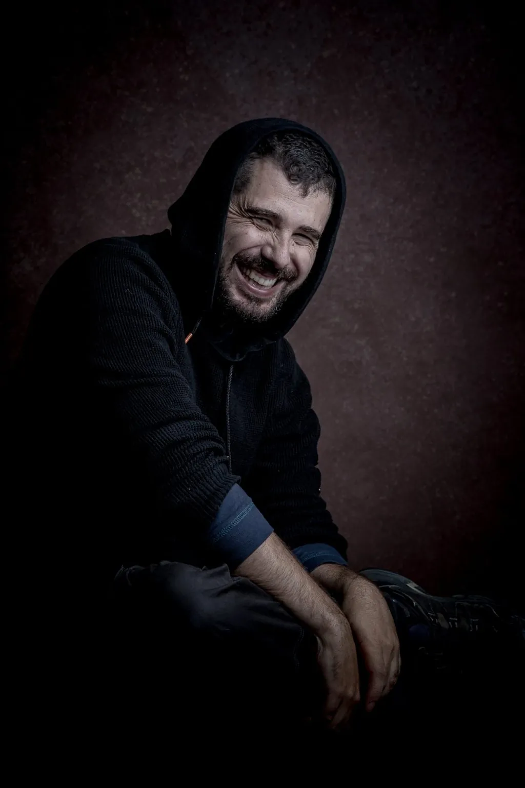 Retrato de Samuel Jiménez Peña, sentado y riendo, con una sudadera con capucha.