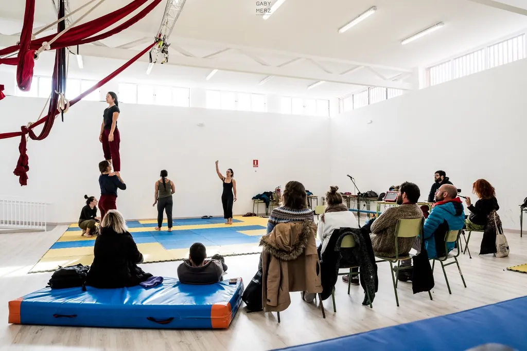 La sala del CECO Comunitario Guatemala: una alumna de pie sobre los hombros de un compañero, telas aéreas colgadas y un grupo de público sentado mirando la muestra.
